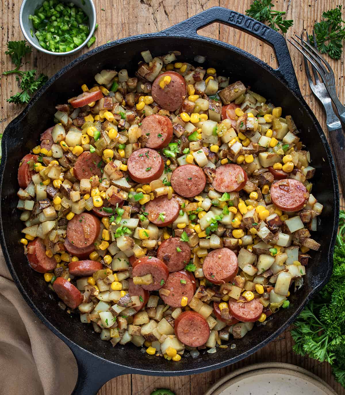 Campfire Hash, also known as kielbasa hash, is a flavorful and hearty dish that brings together a variety of ingredients to create a satisfying one-pan meal. It is a comforting and enjoyable meal loaded with smoked sausage, potatoes, and vegetables, reminiscent of outdoor gatherings and campfire cooking! Skillet of Campfire Hash - Kielbasa Hash on a Cutting Board From Overhead.