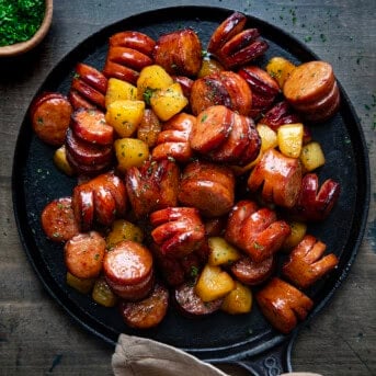 Skillet of Pineapple Hasselback Kielbasa Bites on a dark table from overhead.