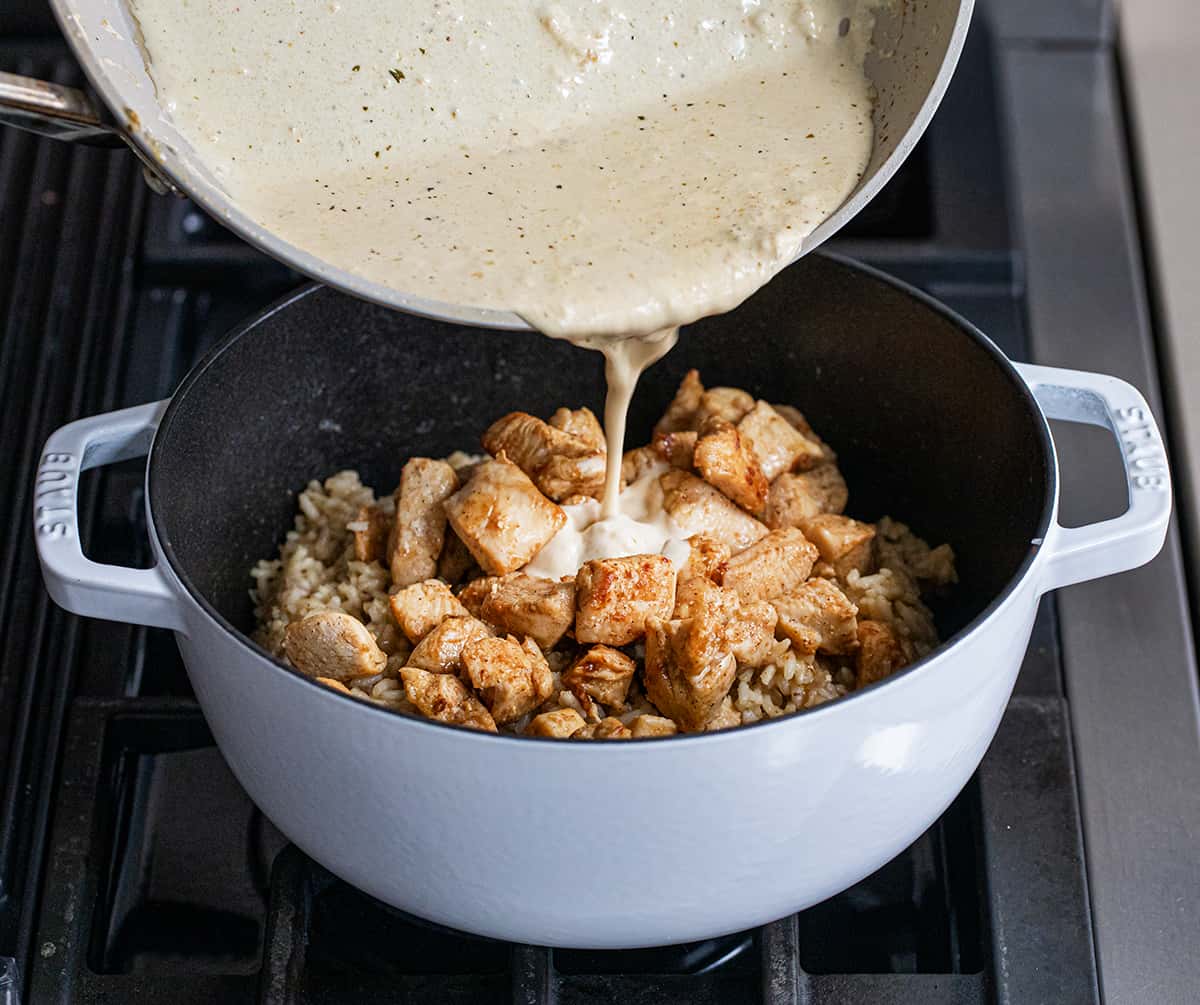Adding sauce to the pot of Cajun Chicken and Rice on the stove.