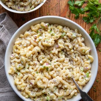 Macaroni Salad in a big bowl with a spoon on a wooden table.