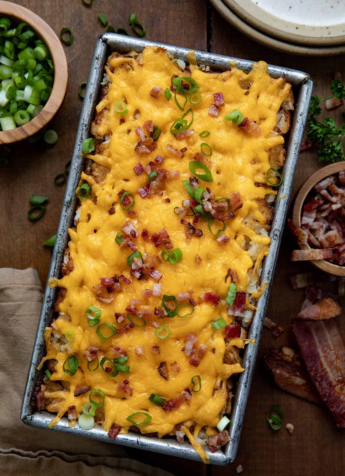 Craving a delicious and filling breakfast? Look no further than this Hash Brown Breakfast Loaf. With layers of hash browns, bacon, sausage, eggs, and cheese, it's the ultimate breakfast comfort food! Hash Brown Breakfast Loaf on a wooden table from overhead.