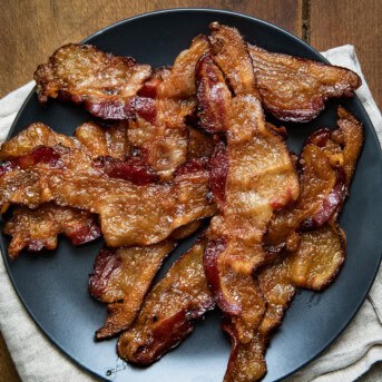 Bacon on a black plate on a wooden table from overhead.