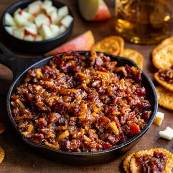 Mini Skillet of Apple Whiskey Bacon Jam surrounded by crackers and diced apples.