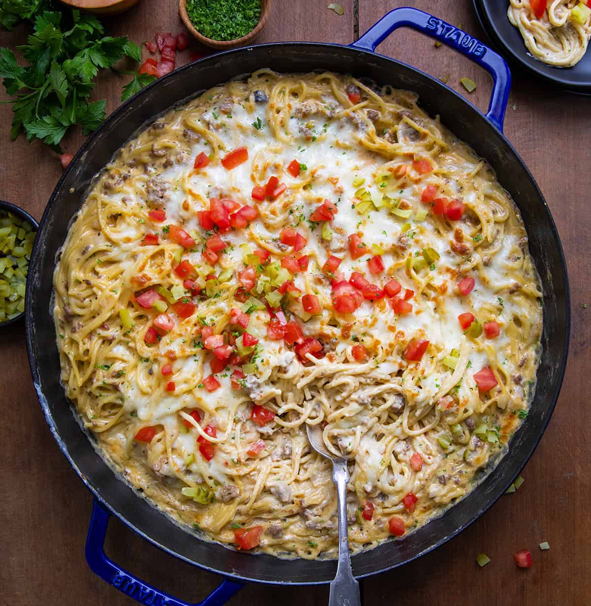 Cheeseburger Tetrazzini is a pasta dish that gives you all of the flavors of a cheeseburger with the creaminess of tetrazzini, topped with melty mozzarella cheese! Skillet of Cheeseburger Tetrazzini on a wooden table with a spoon in it from overhead.
