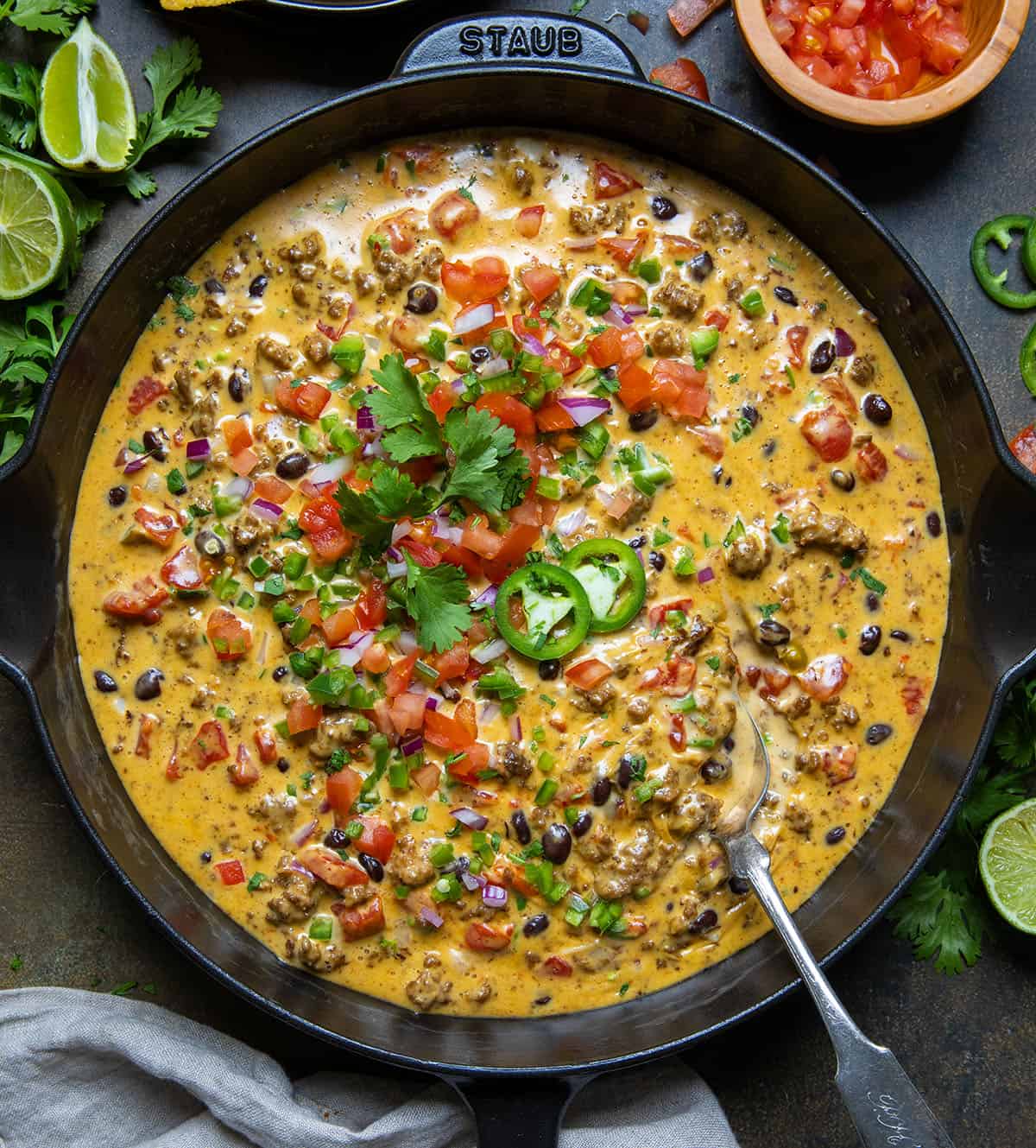 Take your dip to the next level with Cowboy Queso! This flavorful beer cheese dip with ground beef, Pepper jack cheese, and jalapenos is perfect for any occasion! Skillet of spicy Cowboy Queso on a wooden table from overhead.