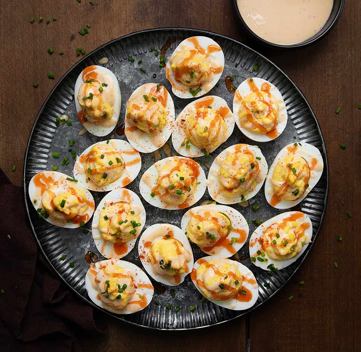 Add a flavorful twist to your appetizers with these Bang Bang Deviled Eggs. Creamy egg yolks mixed with tangy bang bang sauce for a delicious treat! Plate of Bang Bang Deviled Eggs on a wooden table from overhead.