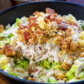 CLose up of a bowl of Chicken Caesar Salad Dip with some of it removed.