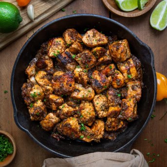 Skillet of Jerk Salmon Bites on a wooden table from overhead.
