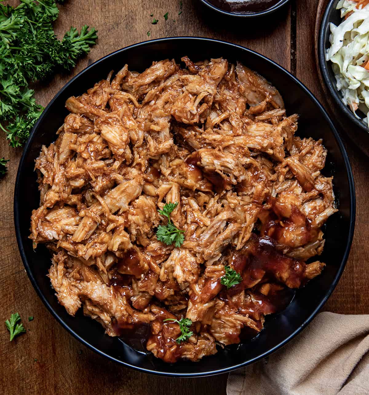 Make delicious Two Ingredient Pulled Pork effortlessly with a slow cooker. Enjoy tender, juicy pork and smoky barbecue flavor! Bowl of Two Ingredient Pulled Pork on a wooden table from overhead.