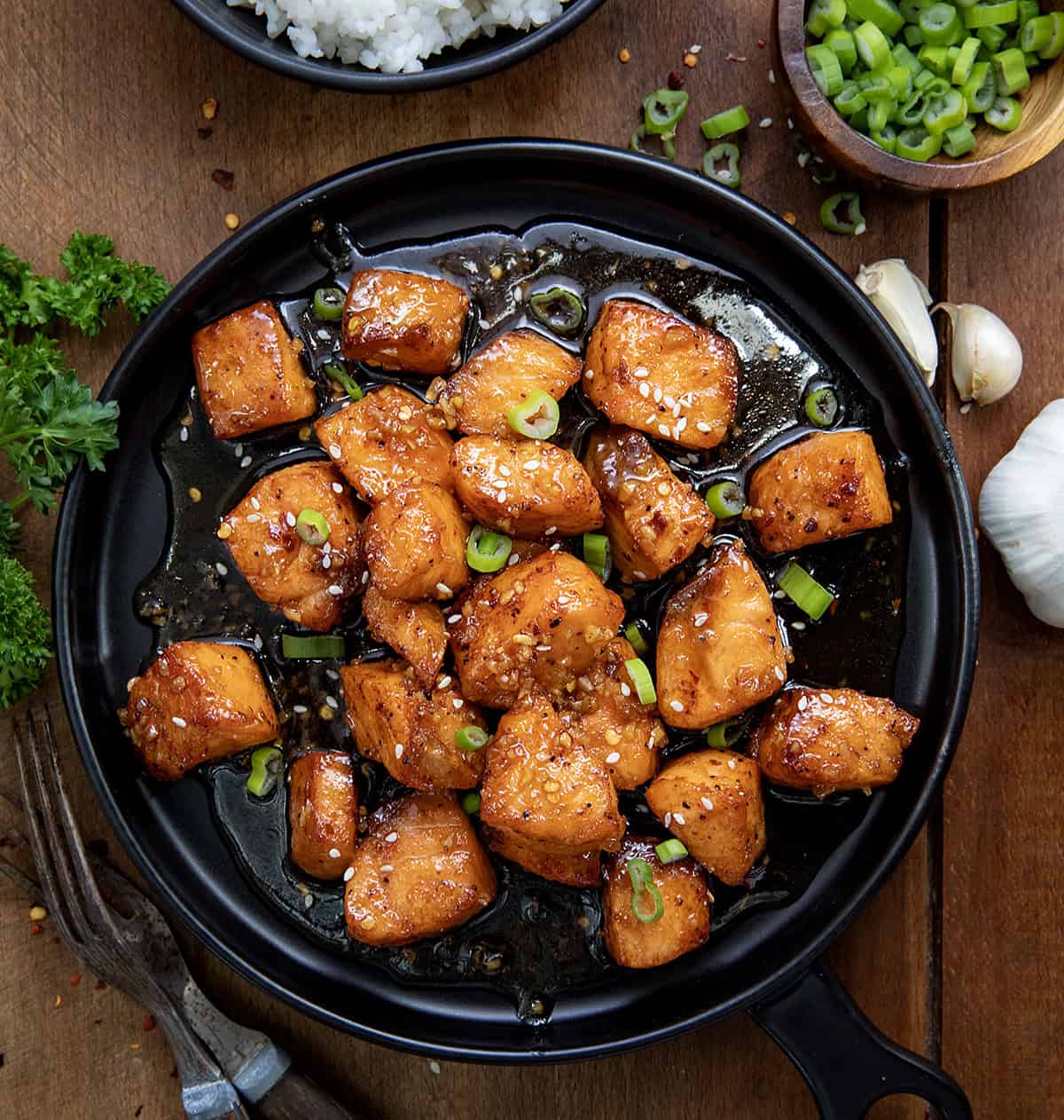Indulge in Honey Garlic Salmon Bites, air-fried to perfection with a buttery glaze and a hint of spice. A must-try dish! Honey Garlic Salmon Bites on a black plate on a wooden table from overhead.