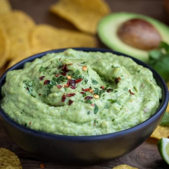 Black bowl of Spicy Avocado Dip on a wooden table.