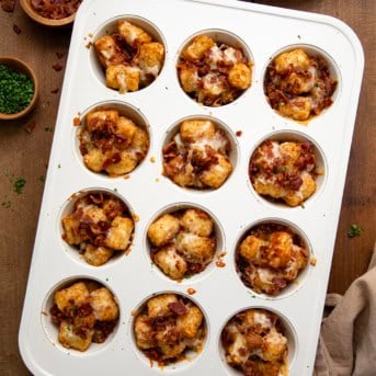 Muffin tray with Bacon Cheddar Tater Tot Bites in it on a wooden table from overhead.