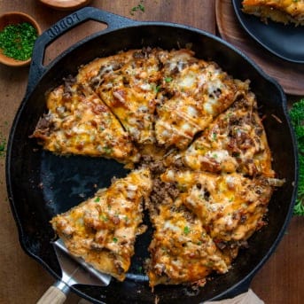 Patty Melt Pizza in a skillet cut into pieces and with a serving spoon in the pan.