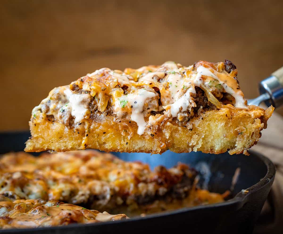 Picking up a pice of Patty Melt Pizza from a skillet.