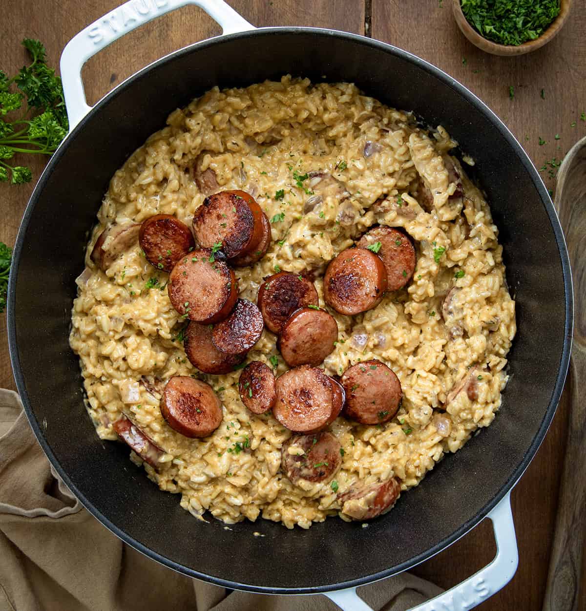Cajun Sausage and Rice is packed with bold Cajun flavors, from the seasoned rice to the sauce, with browned andouille sausage added to the mix for even more of a kick! If you love a dish with a little heat to it, you will love this! Pot of Cajun Sausage and Rice on a wooden table from overhead.