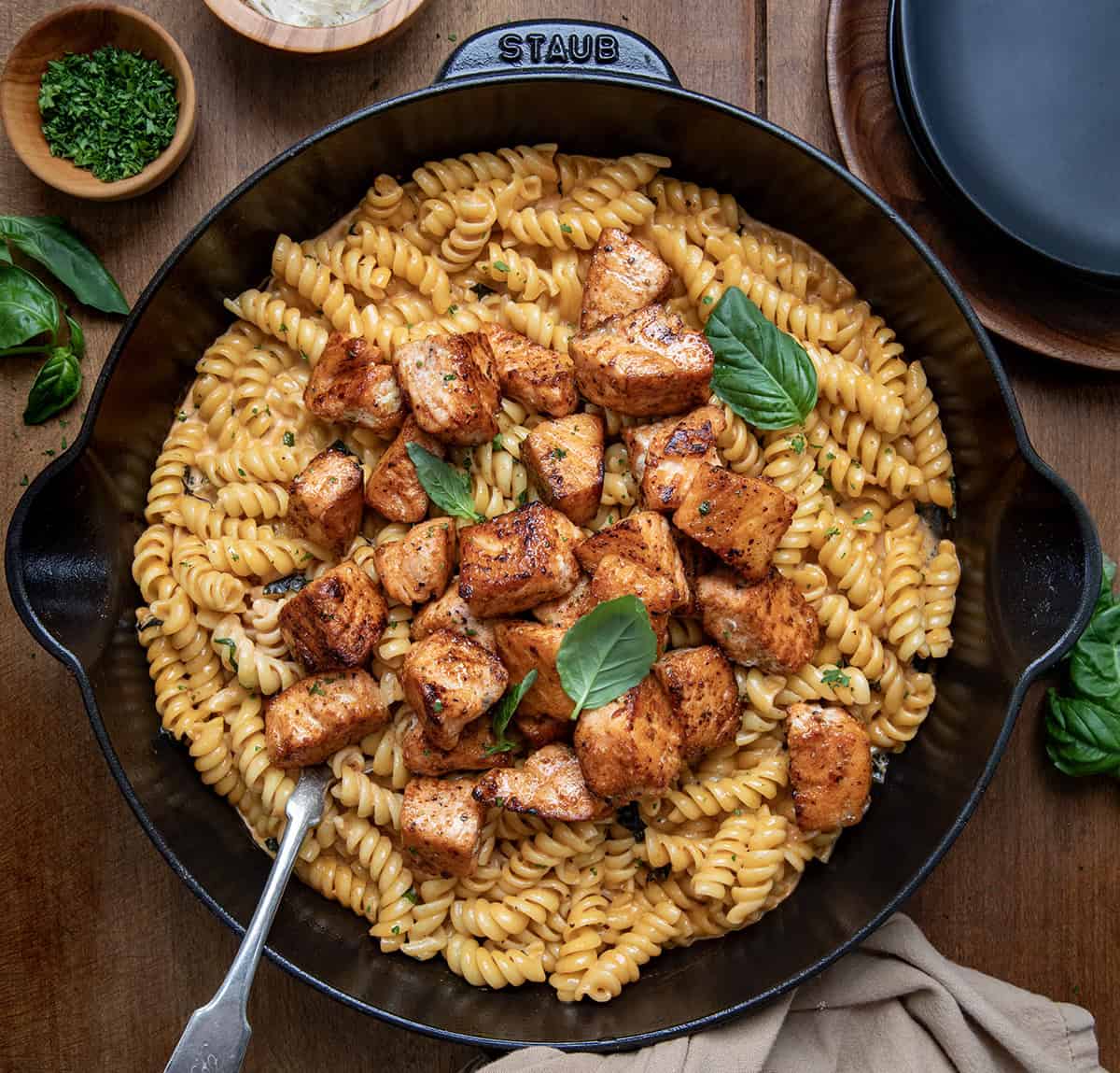 Skillet of Tomato Basil Salmon Pasta with a spoon in it on a wooden table. 